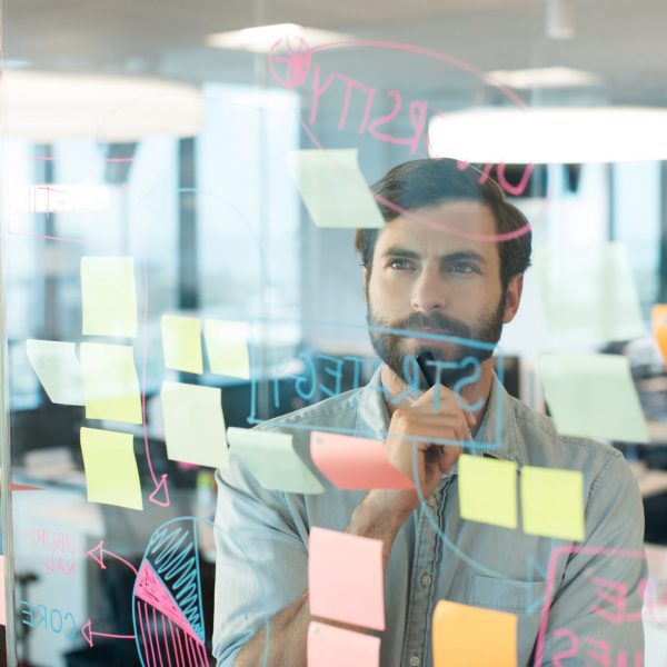 Thoughtful businessman looking at strategy written on glass at office